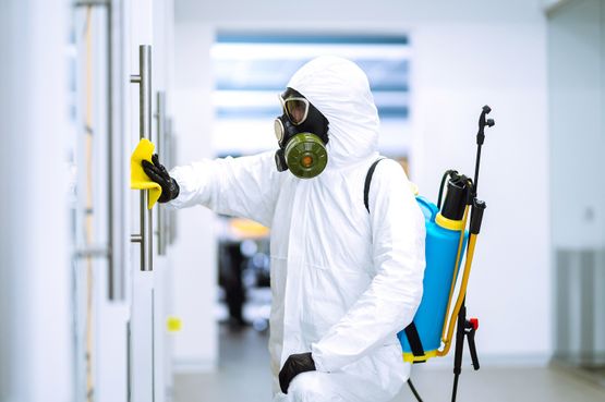 A person in a white protective suit and mask diligently cleans a room, ensuring hygiene and cleanliness.
