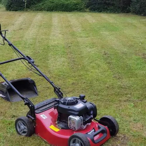 A red lawn mower on the grass, used for grounds maintenance.